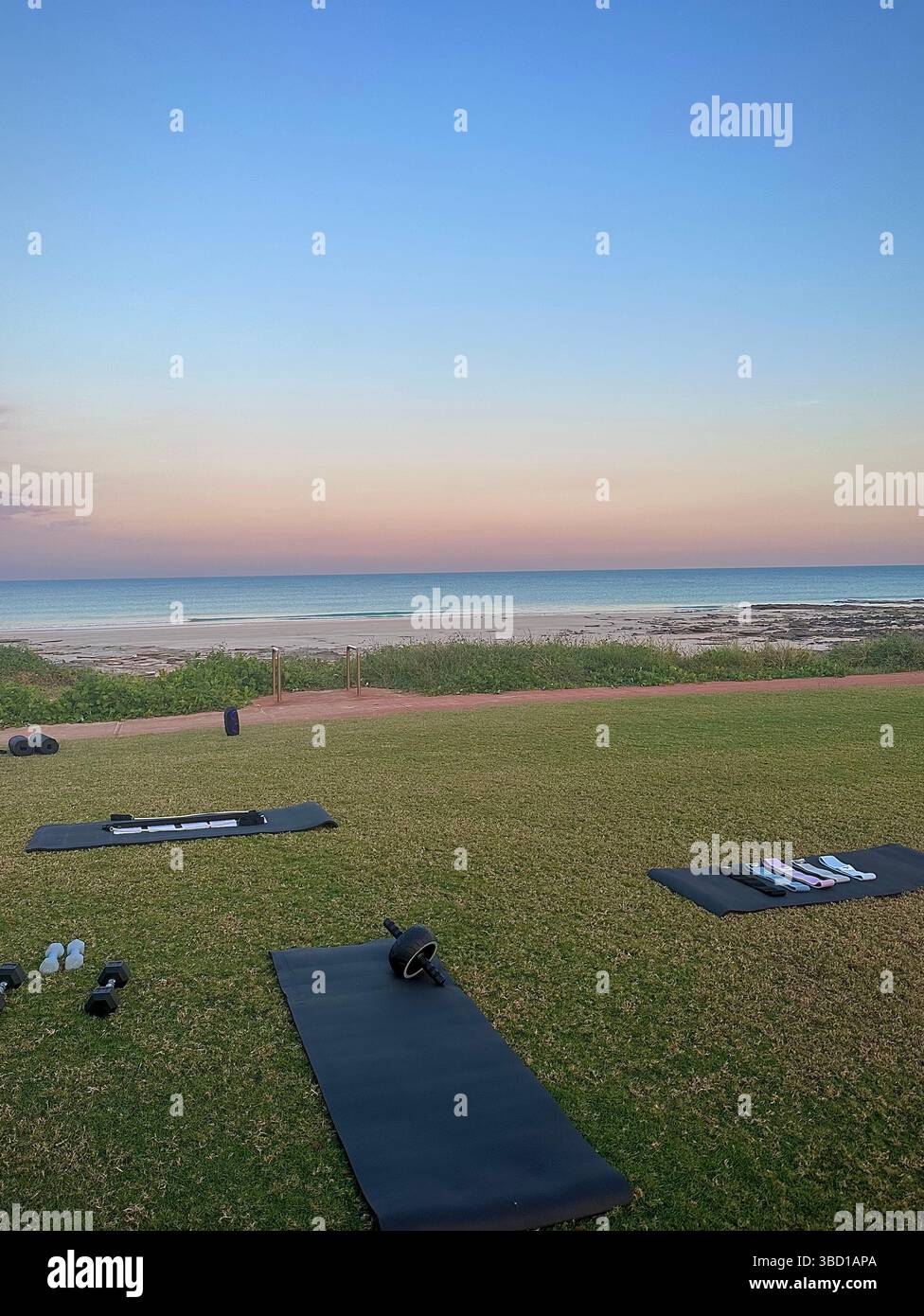 Outdoor-Fitness am Strand bei Sonnenaufgang mit Yogamatten und Gewichten – perfekt für Wellness, Lifestyle und gesundheitsorientierte Konzepte. - Smartphone-aufgenommenes Stockfoto