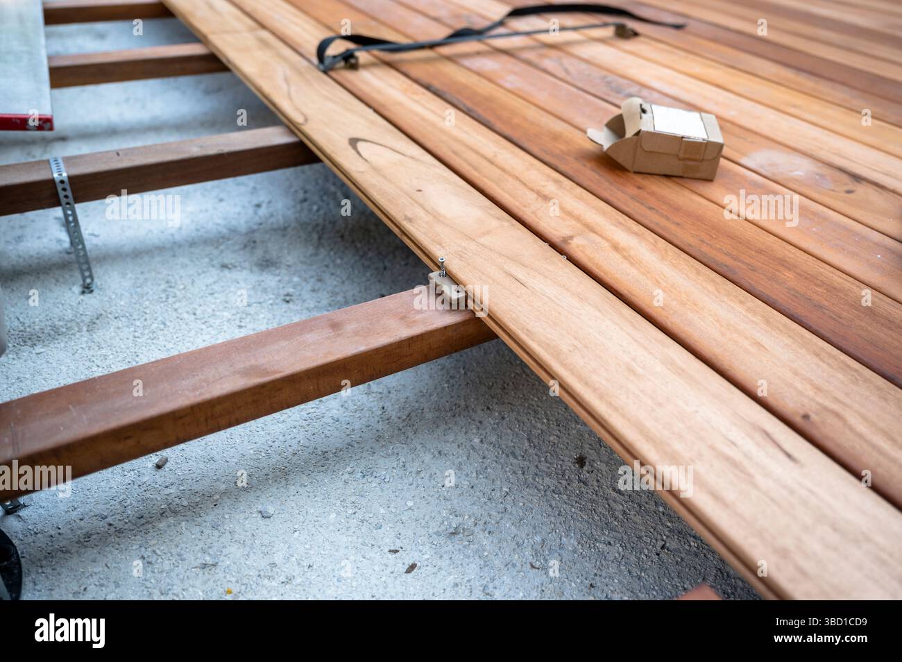 Nahaufnahme der Holzdielen, die mit versteckten Befestigungselementen an einem Hilfsrahmen montiert werden. Die Abbildung zeigt eine Konstruktionsphase mit Werkzeugen und Material Stockfoto
