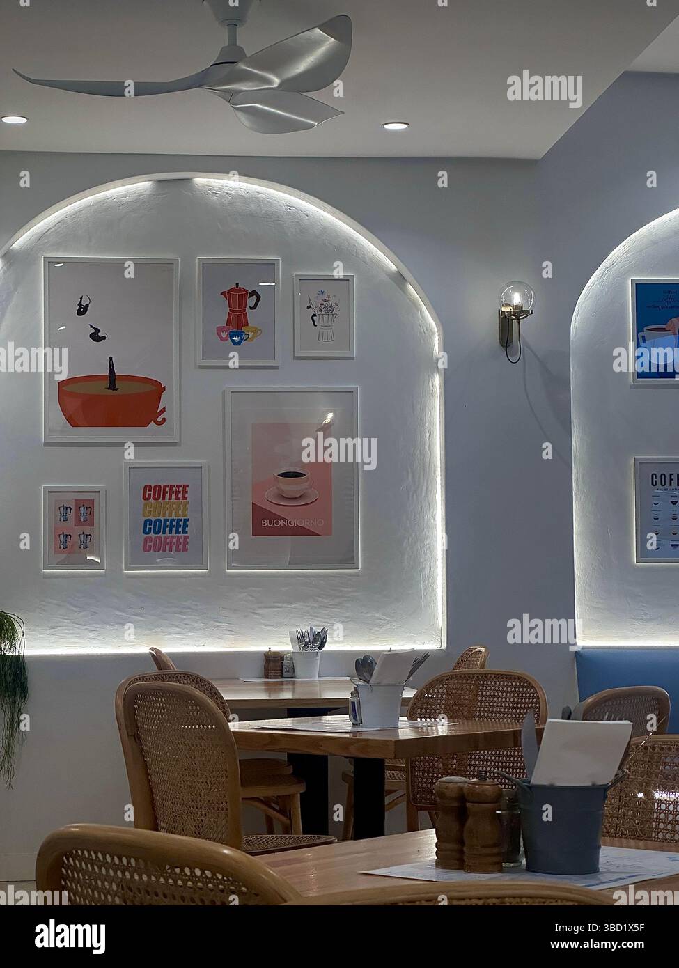 Gemütliches, modernes Café mit Rattanstühlen, gerahmter Kaffeekunst und warmer Beleuchtung schaffen eine entspannte Atmosphäre. - Smartphone-aufgenommenes Stockfoto