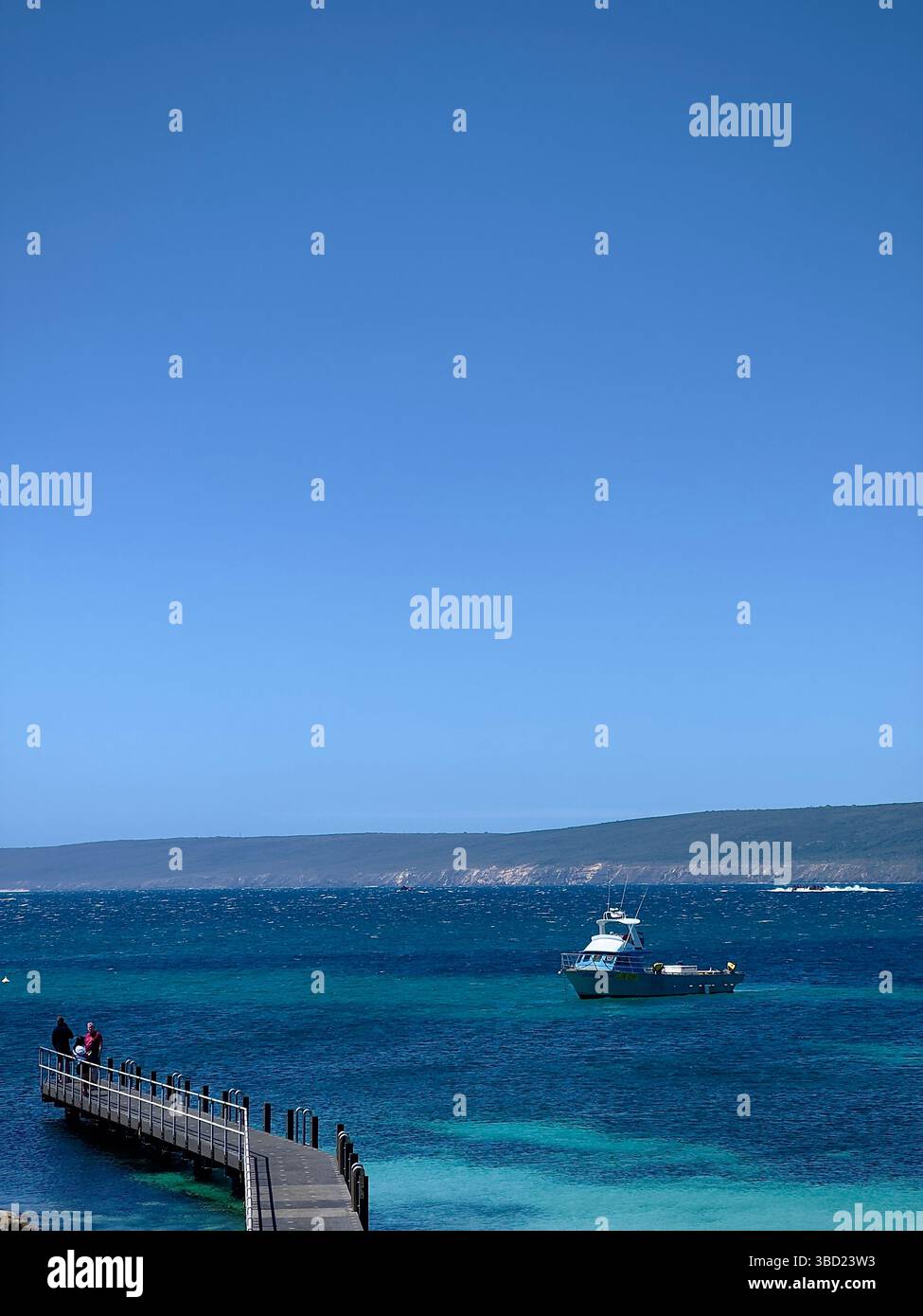 Malerischer Blick auf die Küste eines kleinen Piers und eines vor Anker liegenden Bootes im kristallklaren türkisfarbenen Wasser unter einem hellblauen Himmel, perfekt für Reisen und Tourismus - Smartphone-aufgenommenes Stockfoto
