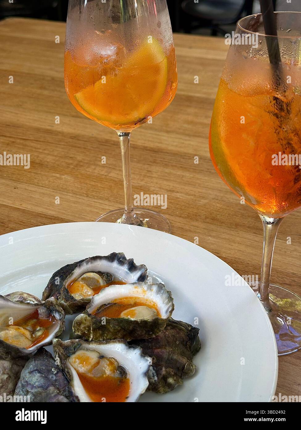 Frische Austern mit würziger Sauce und zwei erfrischenden Aperol Spritz Cocktails, perfekt für ein Sommererlebnis mit Meeresfrüchten. Stockfoto