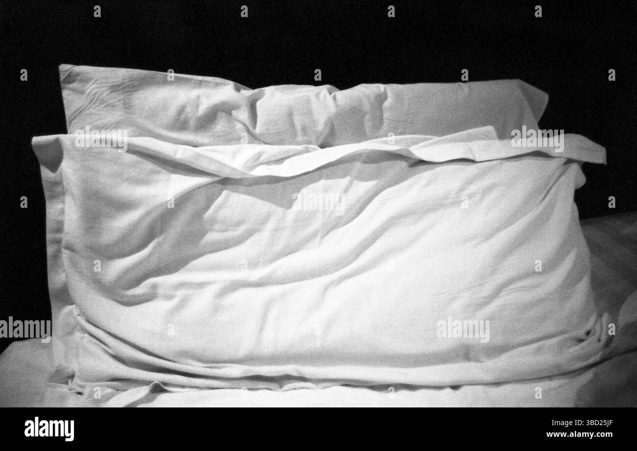 Schwarzweiß-Filmfoto aus den 2010er Jahren von einem ungebauten Bett mit faltigen Kissen Stockfoto