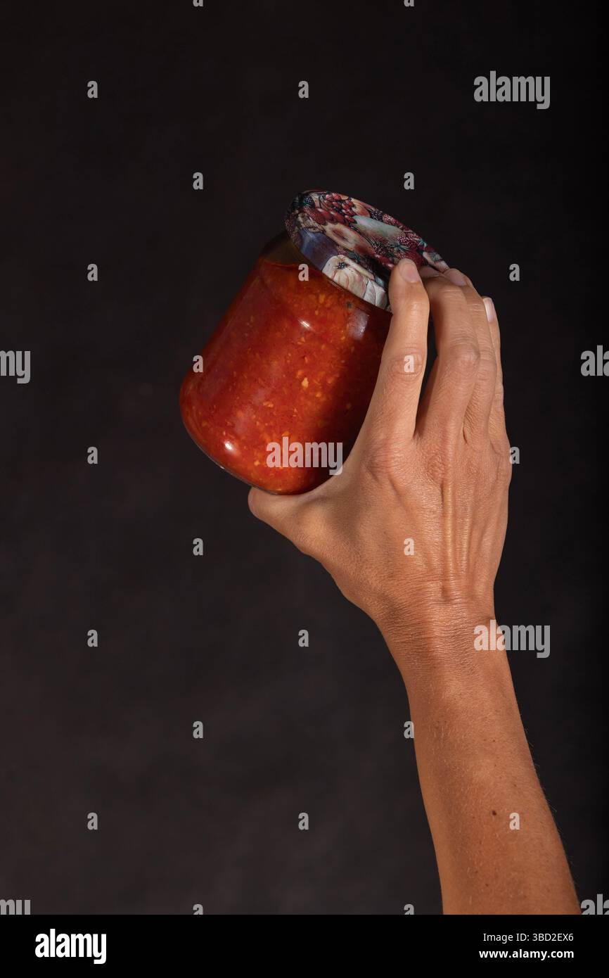 Die männliche Hand hält ein Glas mit hausgemachter Orangengemüsesauce Stockfoto