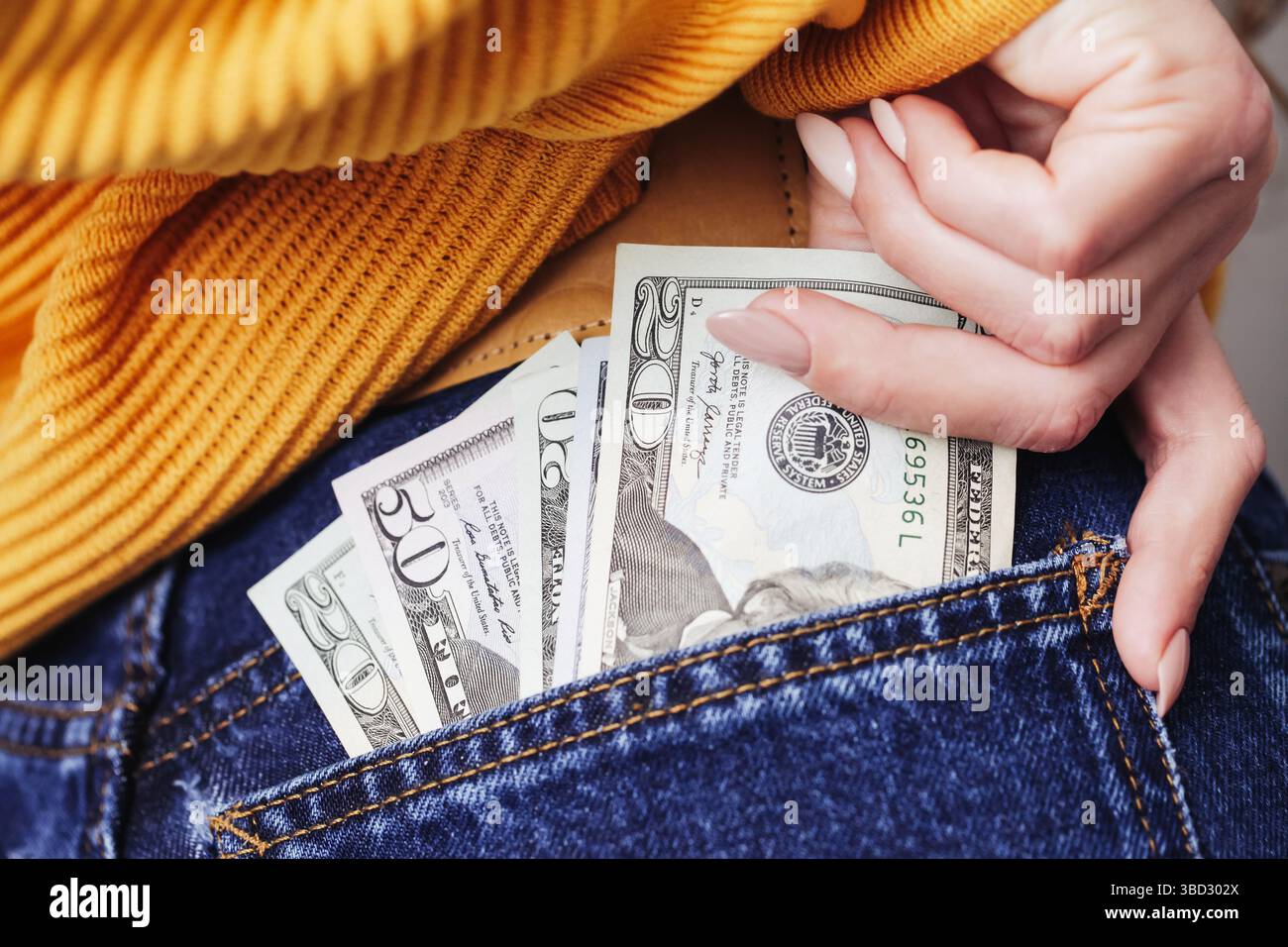 Hand, die Bargeld in die Tasche steckt. Geld in Jeans versteckt. Dollarscheine aus nächster Nähe. Konzept der Spareinlagen und Finanzierung. Symbol der wirtschaftlichen Freiheit. Persönlicher Reichtum. Stockfoto