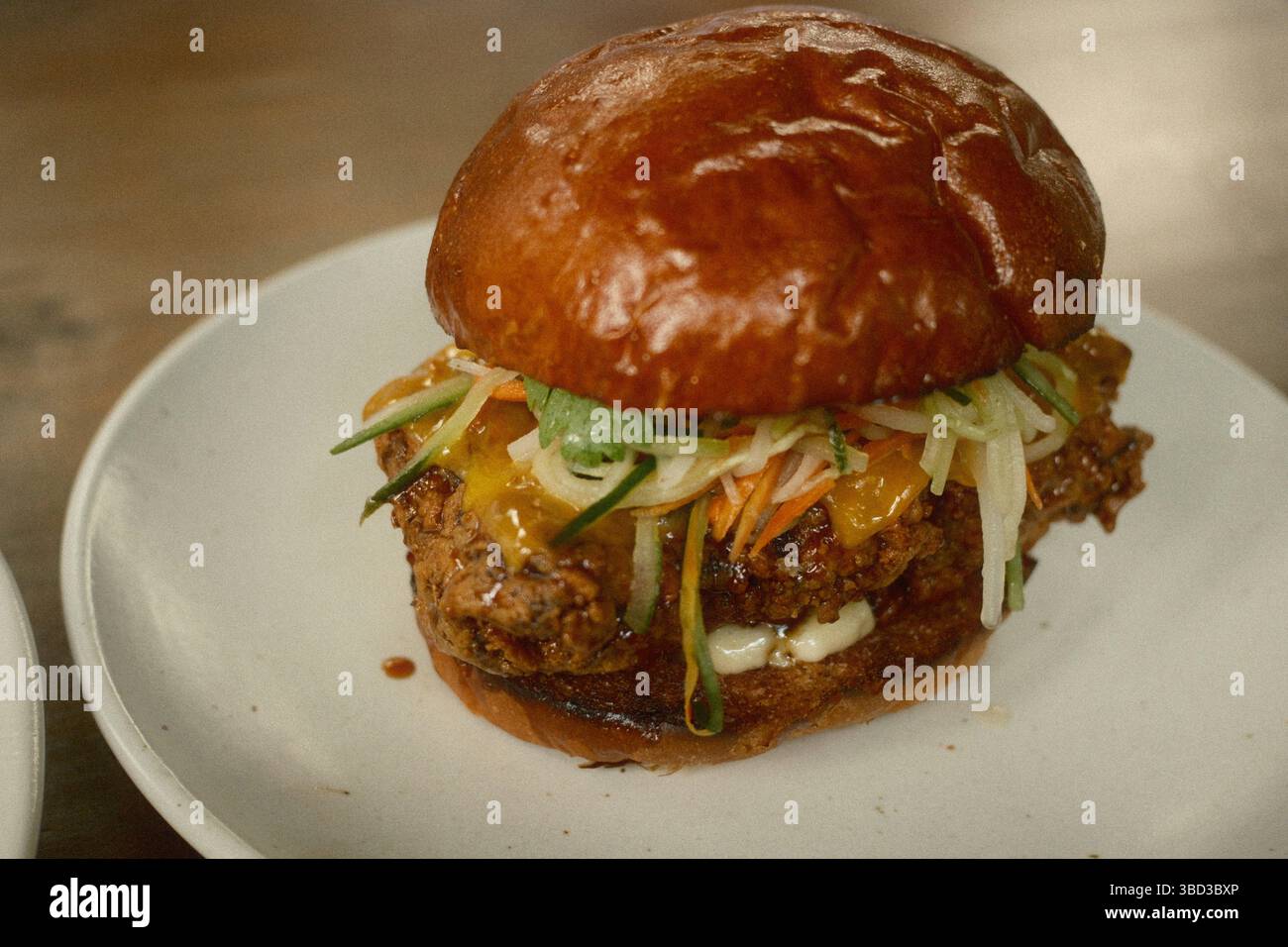 Knusprig gebratenes Hühnerschenkel-Burger-Brötchen mit Karamellglasur, Mayonnaise, Cheddar und Gurken Stockfoto