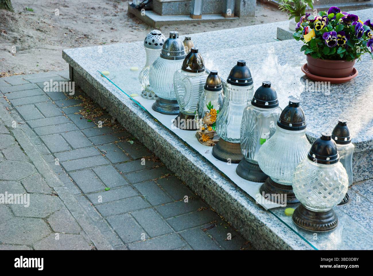 Eine Reihe von Laternen auf dem Granitgrab, dekoriert mit leuchtenden Blumen auf dem Friedhof, schaffen eine ruhige und reflektierende Atmosphäre. Stockfoto