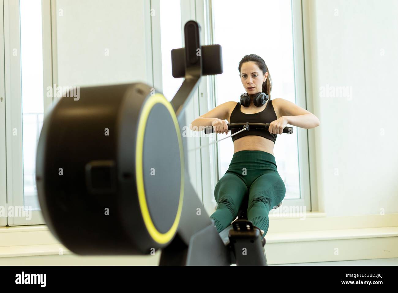 Eine entschlossene Frau rudert in einem hellen, stilvollen Fitnessstudio, zeigt ihre Kraft und konzentriert sich auf ihre Fitness-Reise. Stockfoto