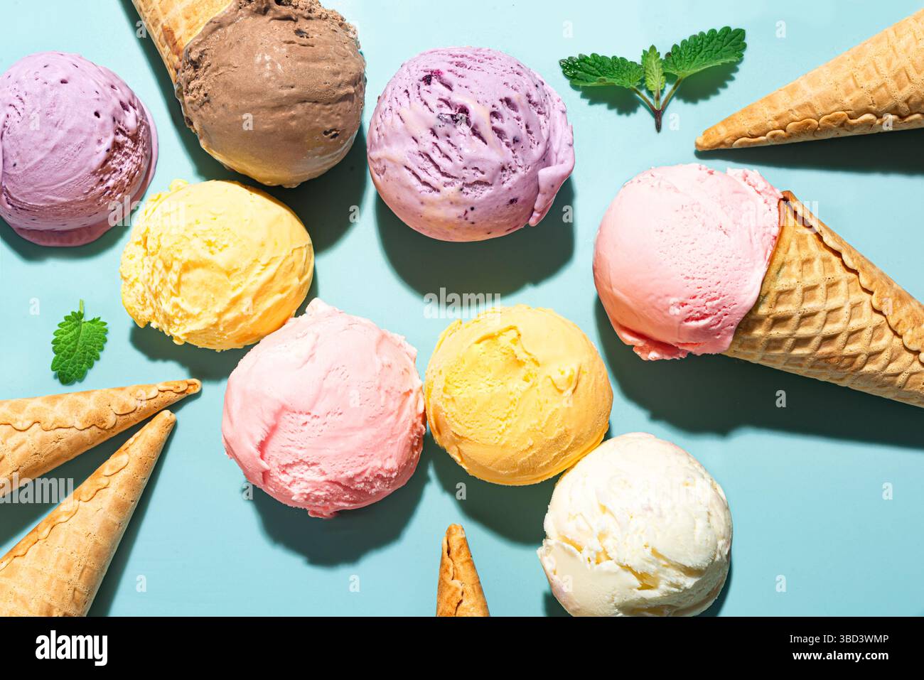 Verschiedene Eiskugeln auf blauem Hintergrund, Draufsicht. Verschiedene Eissorten oder Eis mit Waffelkegel, gesundes Sommerdessert kreatives Konzept. Stockfoto