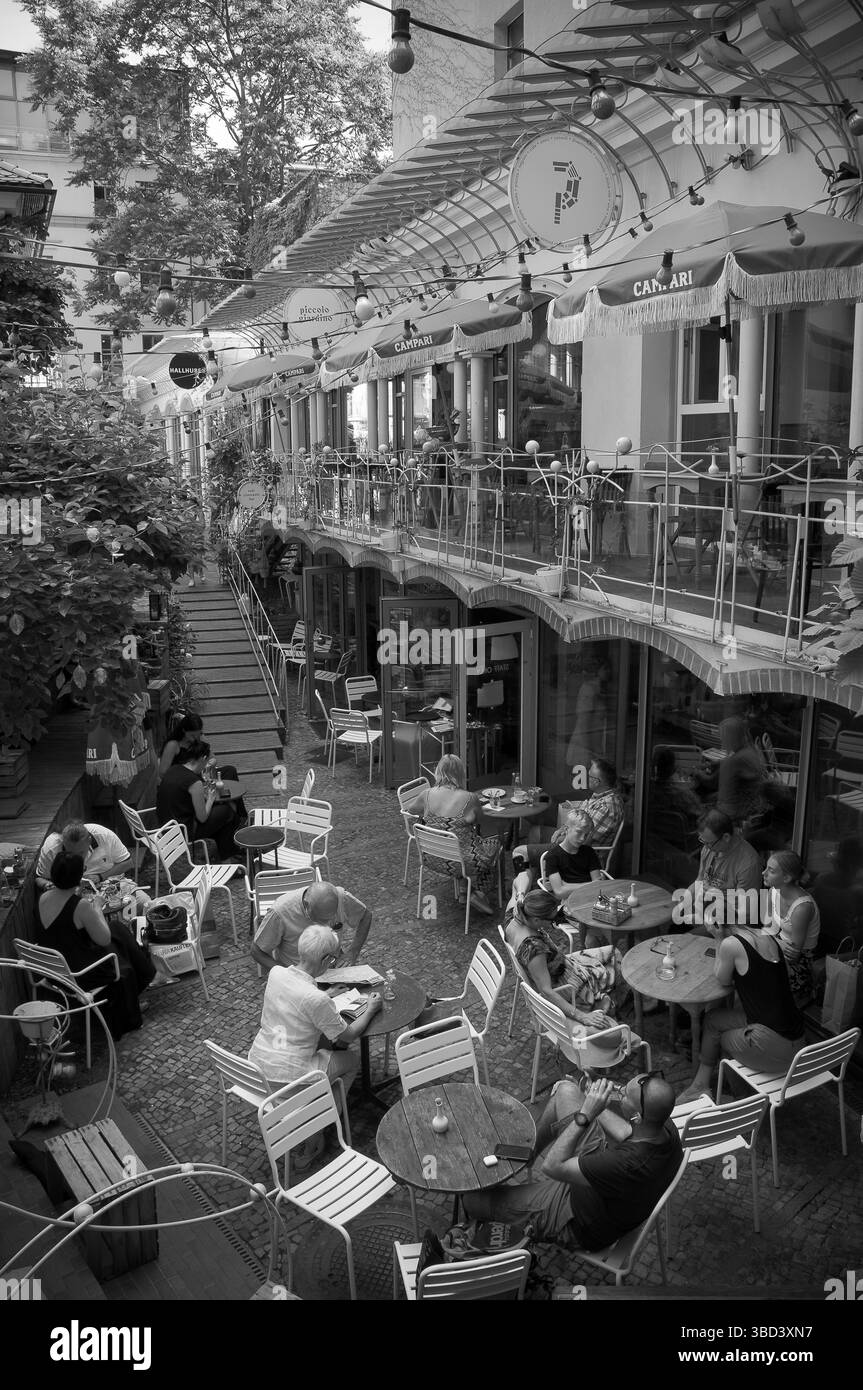 Die Besucher treffen sich an Tischen im fröhlichen Berliner Innenhof, unterhalten sich und genießen gemeinsam das warme Wetter. Stockfoto