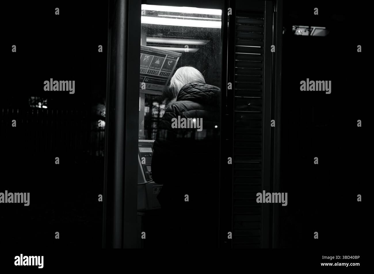 Eine Einzelfigur mit weißem Haar beugt sich über das Telefon in einem schwach beleuchteten Tokio-Stand Stockfoto