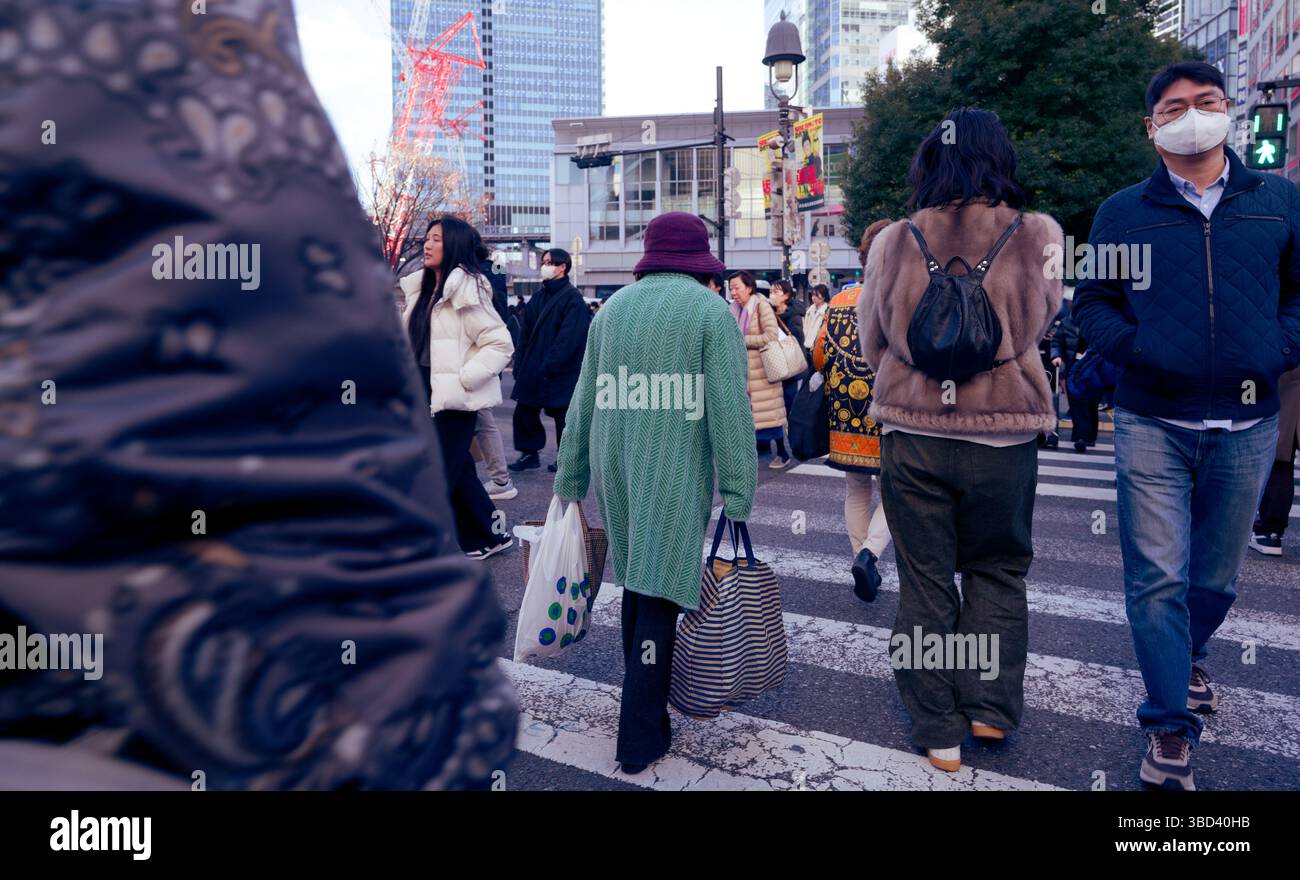 Ältere Frau im grünen Fell überquert Shibuya Crossing inmitten einer hektischen Menge Stockfoto