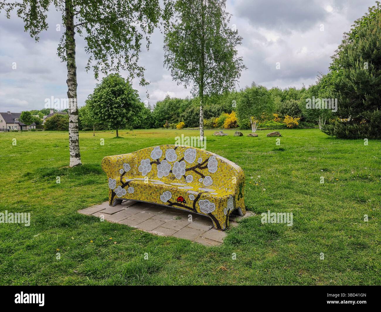 Helle gelbe Steinbank mit Mosaik (Blumenmuster) auf einem grünen Grasfeld in einem Park in den Niederlanden - Smartphone-aufgenommenes Stockfoto