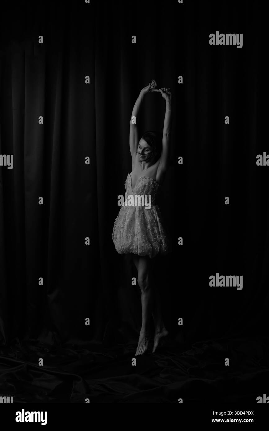 Hellhäutige Ballerina auf Zehenspitzen, Arme hoch. Anmutige Pose mit Eleganz und langen Beinen. Stockfoto
