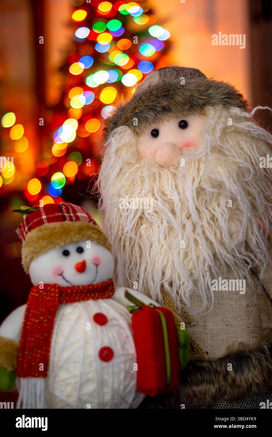 Frosty The Snowman und Santa Claus Figuren zusammen mit den Lichtern eines Weihnachtsbaums im Hintergrund Stockfoto