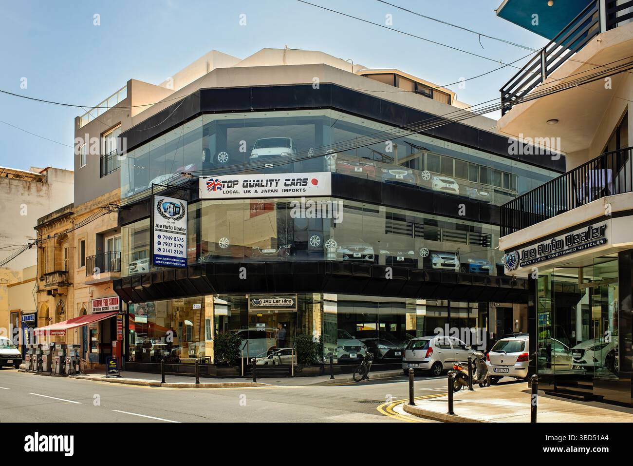Mosta, Malta- 05.21.2025: Joe Auto Dealer Showroom in Malta mit Importwagen aus Großbritannien und Japan. Gebäude mit Glasfassade und Straßenreflexen, geparkte Autos Stockfoto