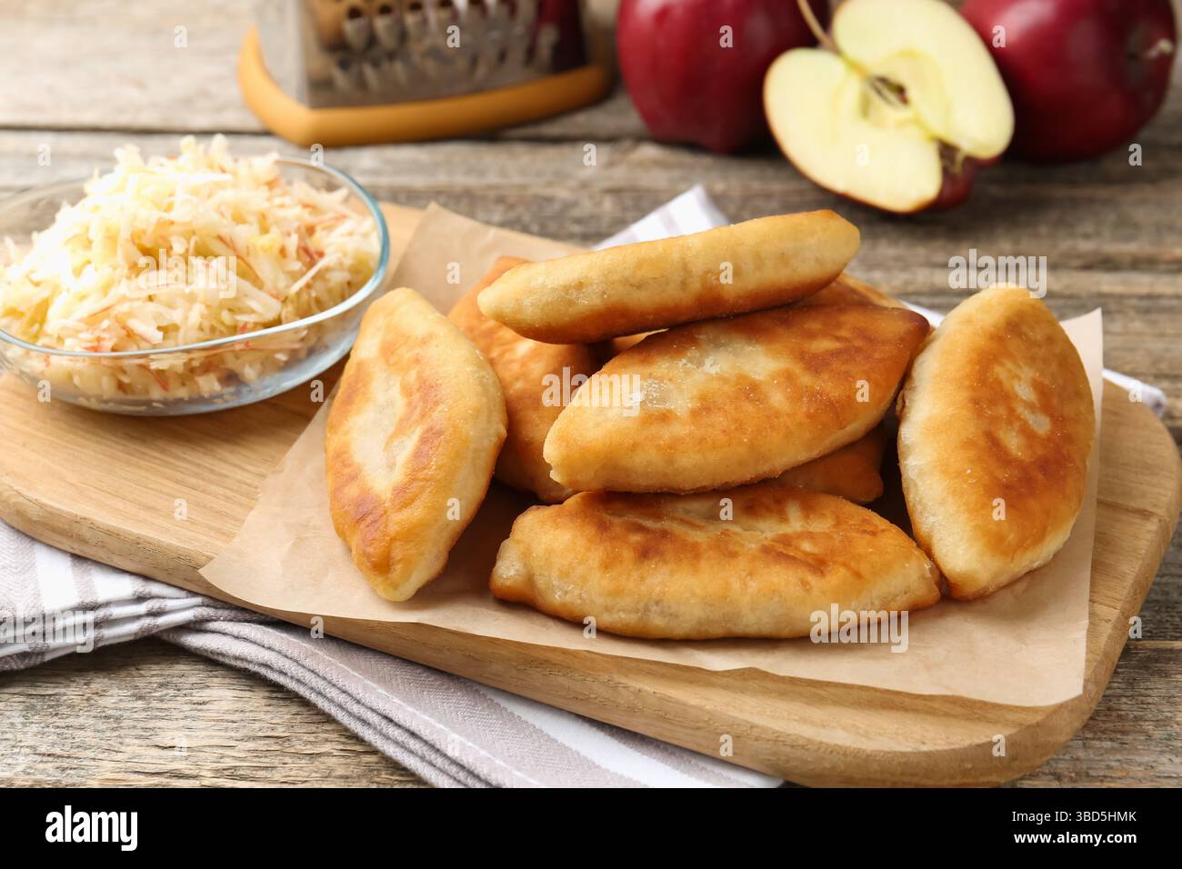 Köstliche gebratene Pyrizhky (gefüllte Kuchen) und Äpfel auf Holztisch, Nahaufnahme Stockfoto Köstliche gebratene Pyrizhky (gefüllte Kuchen) und Äpfel auf Holztisch, Nahaufnahme Stockfoto