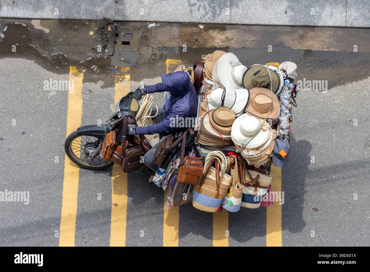 Ein Motorrad mit einer Vielzahl von Hüten und Waren fährt auf einer Stadtstraße in Vietnam Stockfoto