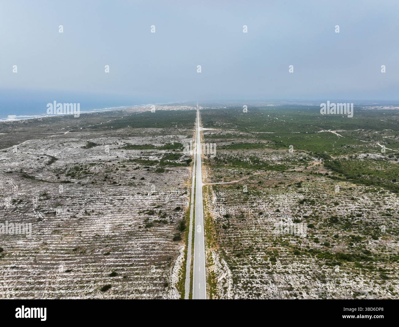 Portugal - Drohnenfoto einer geraden Atlantikstraße, die sich in Richtung einer Küstenstadt und des Atlantischen Ozeans erstreckt Stockfoto