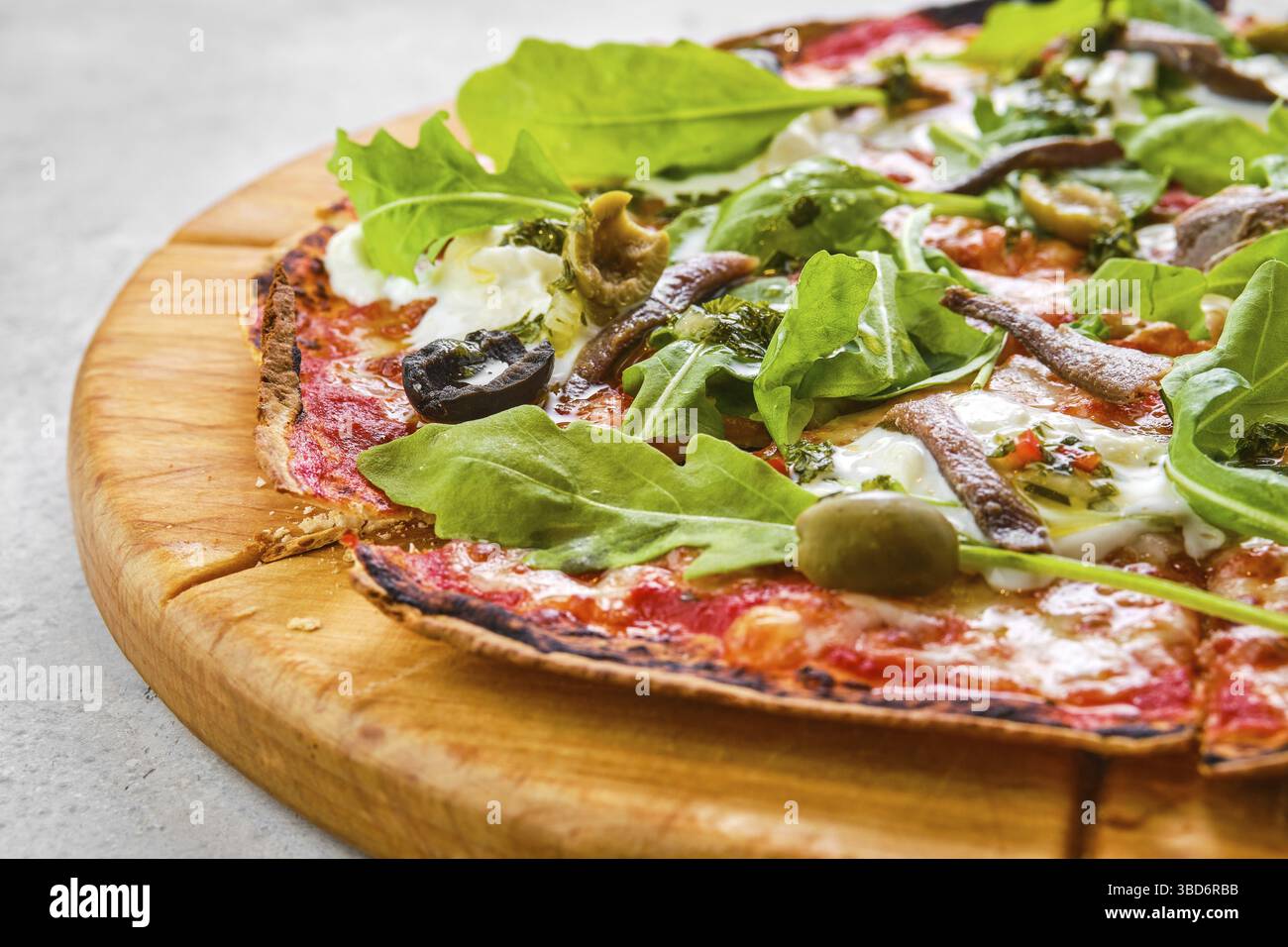 Dünnkrustiger Pizzateig mit Sardellen, Oliven und Stracciatella-Käse (Nahaufnahme mit geringer Schärfentiefe) Stockfoto