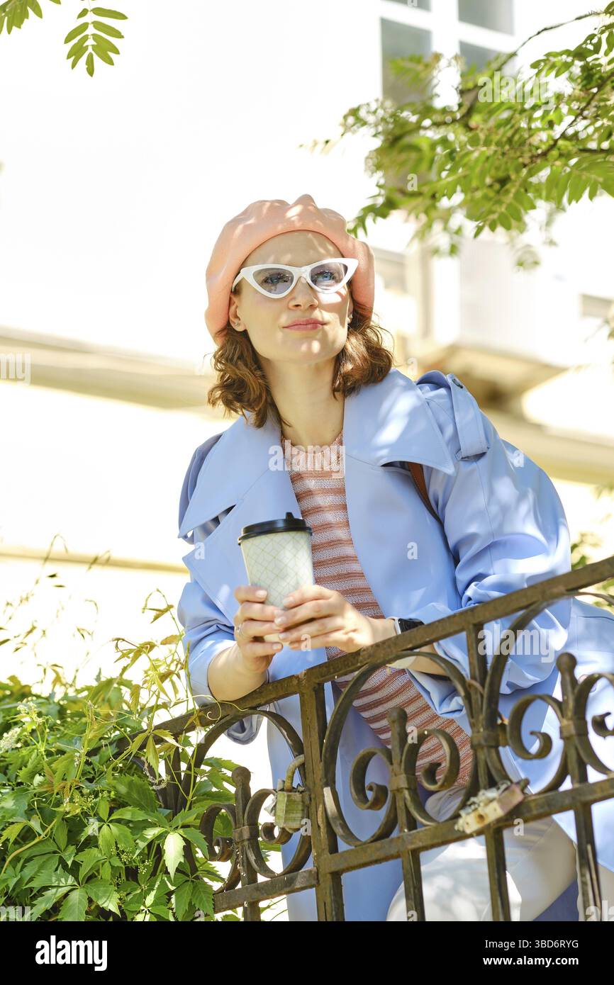 Attraktive Frau mit einem Glas Kaffee zum Mitnehmen versteckt im Schatten im Stadtpark Stockfoto