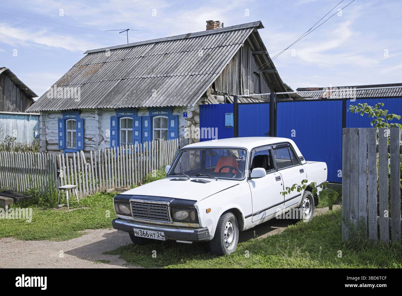 Traditionelles Holzhaus mit weißem Auto, Lada Riva, Lada Nova in einem ländlichen Dorf in Südsibirien, Russland Stockfoto
