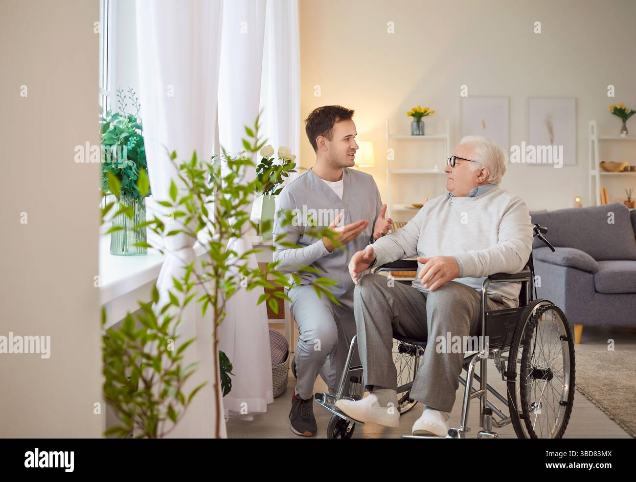 Junger Sozialarbeiter im Gespräch mit älteren behinderten Menschen im Rollstuhl. Stockfoto