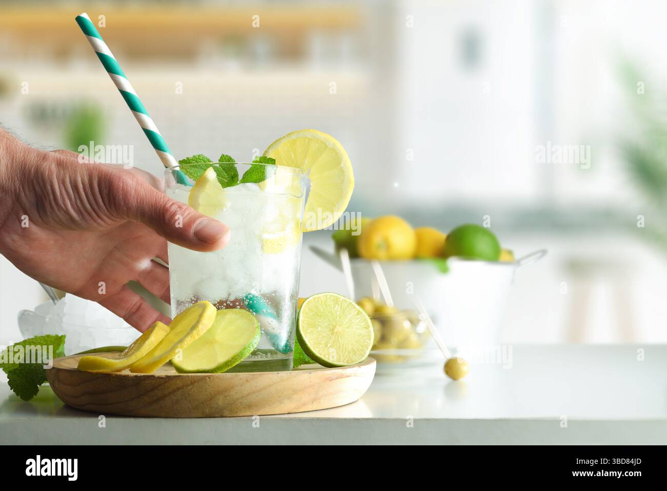Eine Person trinkt Limette mit Limette und Zitrone und viel Eis auf einer weißen Küchenbank, die mit Zitronen- und Limettenscheiben und Fruchtstücken und k dekoriert ist Stockfoto
