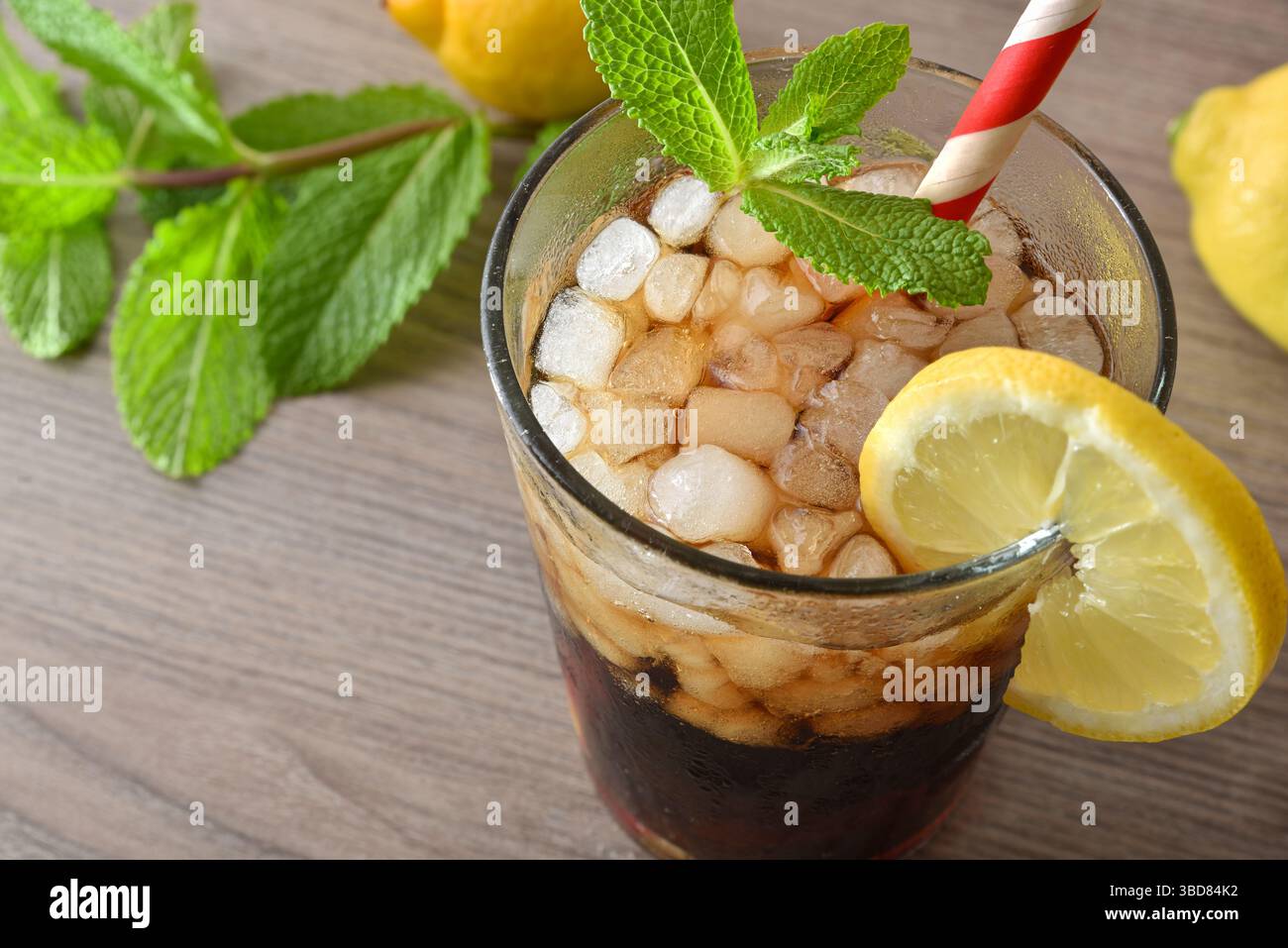 Cocktail auf Cola-Basis mit Minze und Zitrone in einem Glas auf einem Holztisch, dekoriert mit Eis, Minzblättern, Zitronen und einer Dose Cola. Von oben erhobene Aussicht. Stockfoto