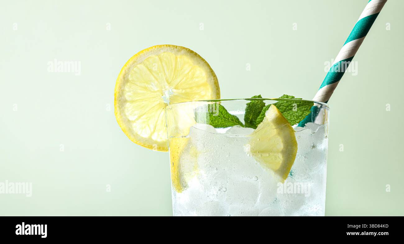 Sehr kaltes Limettenalkoholgetränk mit Eiswürfeln in einer Glasschale mit Minzblättern und einem Strohhalm mit grünem isoliertem Hintergrund. Vorderansicht. Stockfoto