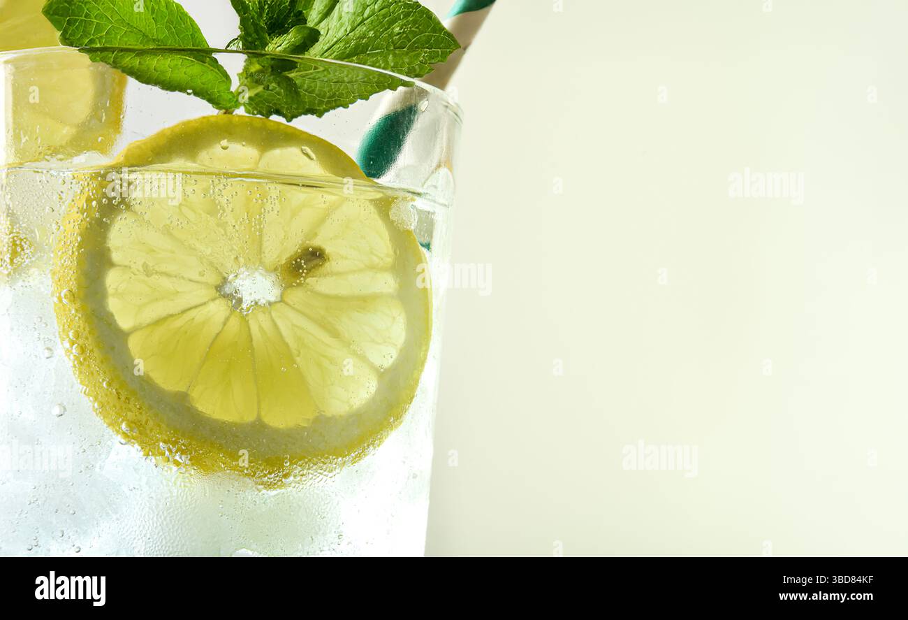 Makroglas aus Glas mit erfrischendem Getränk mit Zitrone und Eis dekoriert mit Minze und einem grünen und weißen Strohhalm mit grünem isoliertem Hintergrund. Vorderansicht Stockfoto