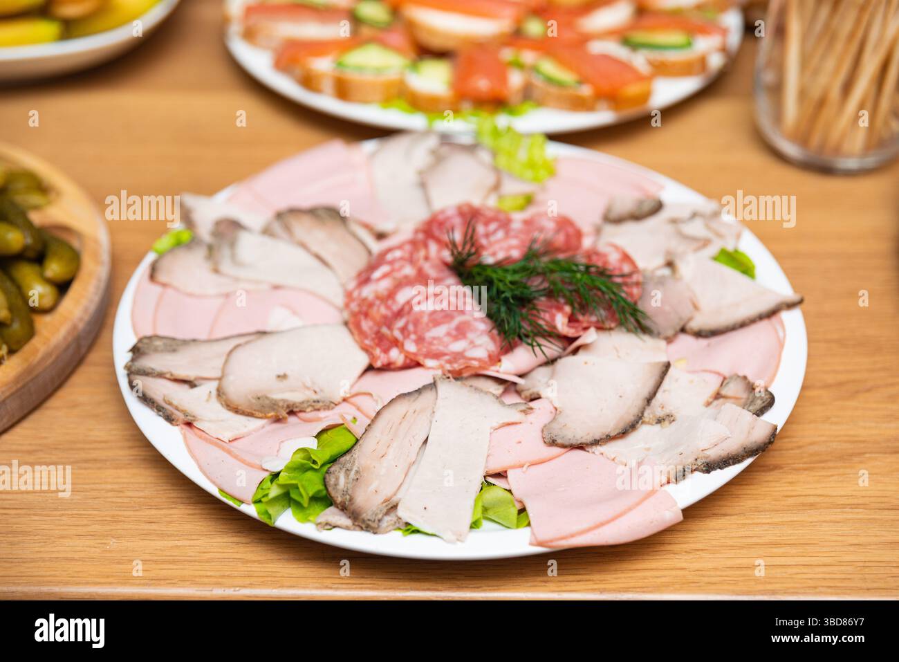 Platte mit in Scheiben geschnittenem Fleisch einschließlich Salami, Schinken und Schweinebraten, garniert mit Dill und Salat für die Party. Stockfoto