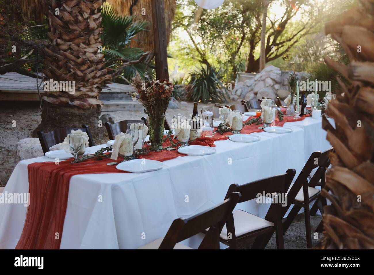 Rustikaler Banketttisch im Freien mit roten Akzenten und Kerzen. Stockfoto