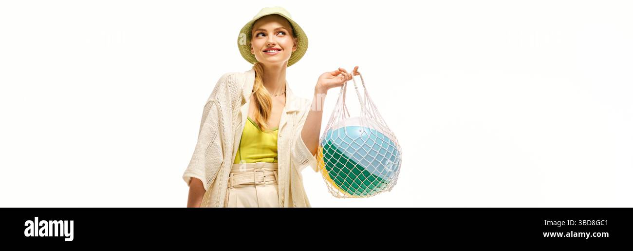 Eine junge Frau in stilvollen Sommerkleidern trägt gerne einen Strandball. Stockfoto