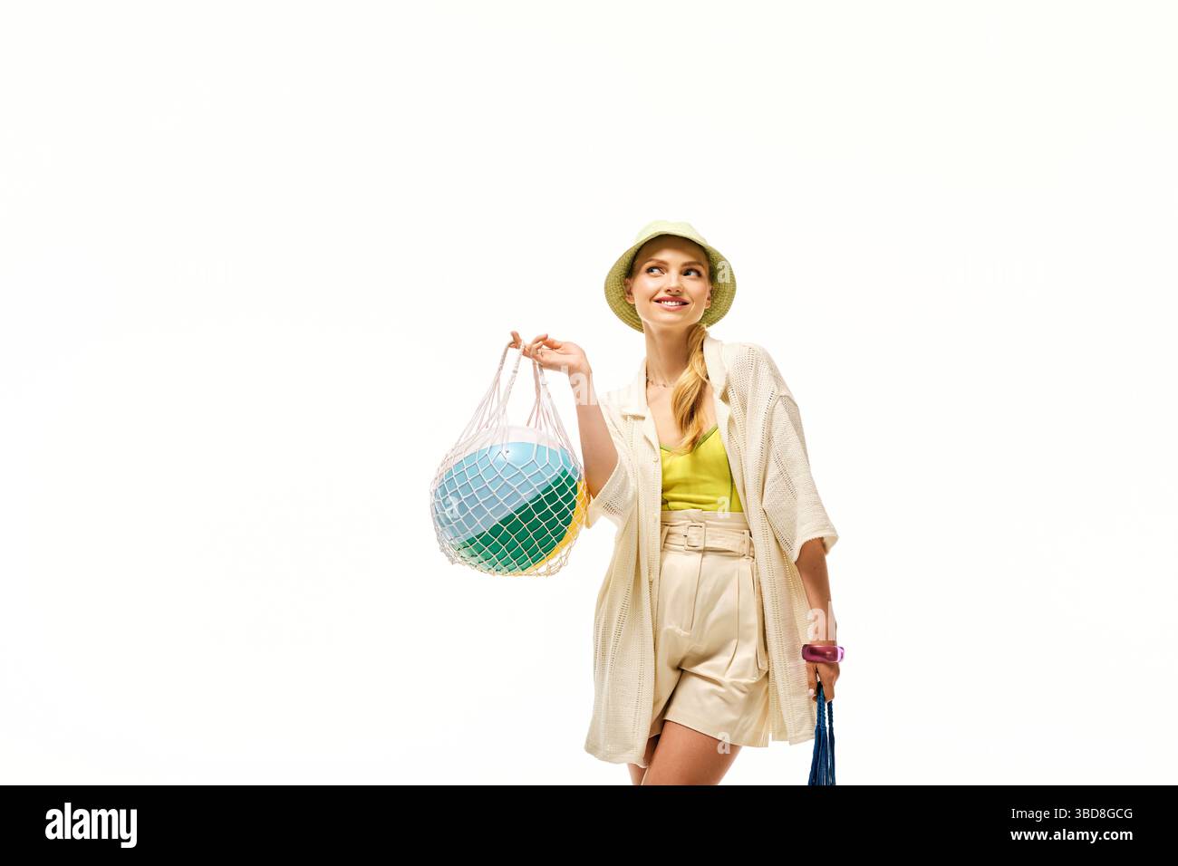 Fröhliche junge Frau in stilvoller Sommerkleidung trägt einen verspielten Strandball und lächelt. Stockfoto