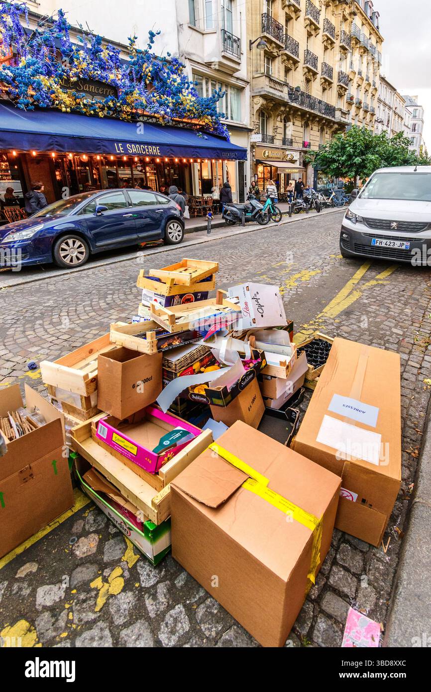Leere Kartons und Kartons stapeln sich auf der Straße und warten auf die Abholung durch die Stadtreinigungsabteilung - Rue des Abbesses, Paris 75018, Frankreich. Stockfoto