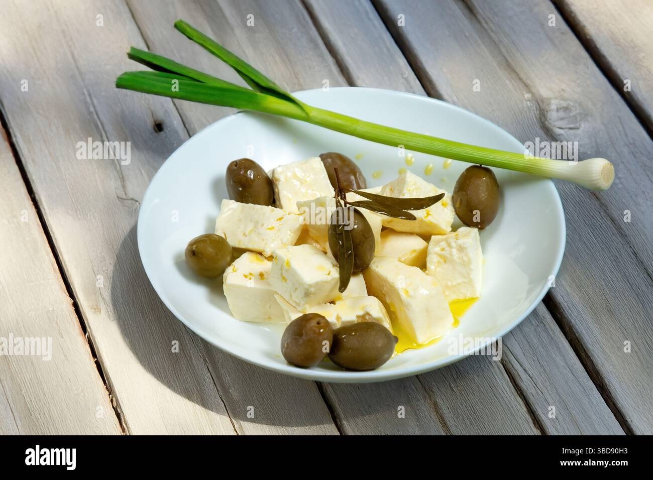 Ein weißer Solekäse und Oliven wurden mit extra nativem Olivenöl übergossen und grüner Knoblauch lag am Rand der Schüssel. Stockfoto