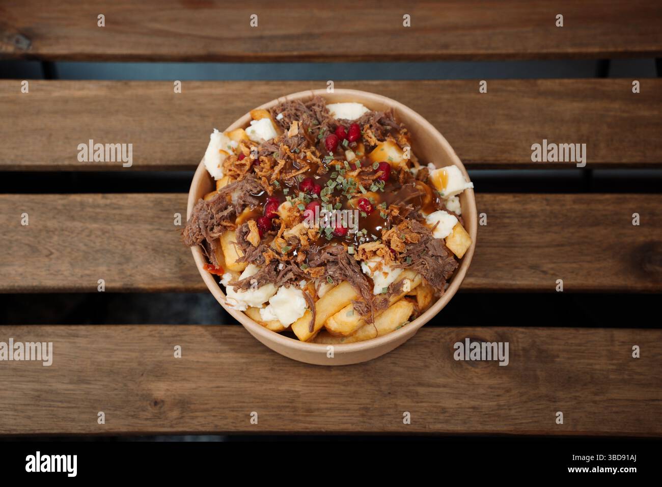 Poutine-Pommes mit Käse und Schweinefleisch in einem Papierbehälter zum Mitnehmen. Köstliche frisch zubereitete Mahlzeit, perfekt für Menüs, Restaurants oder Essenslieferungen Stockfoto