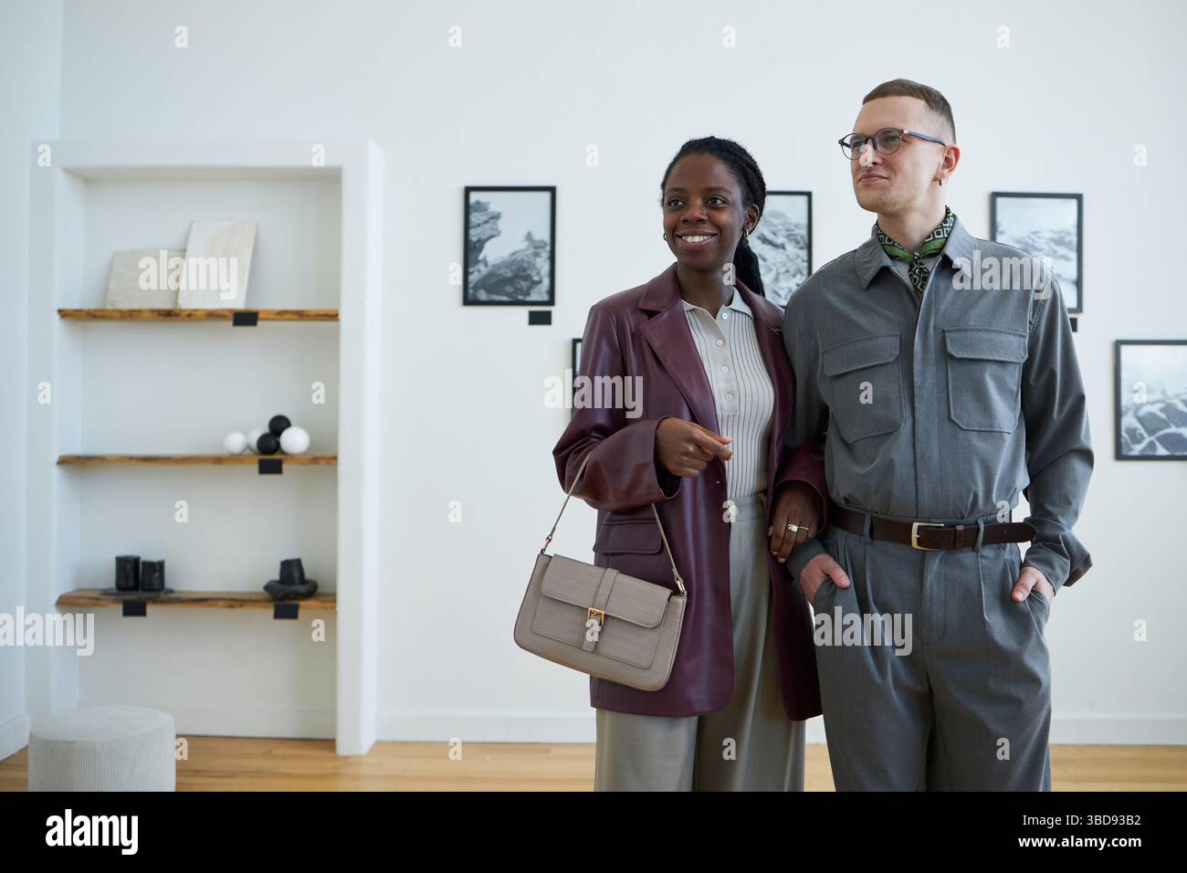 Porträt einer Afrikanerin neben dem kaukasischen Mann in moderner Galerieretage. Beide sind lächelnd und stilvoll gekleidet, mit Kunstwerken, die in t sichtbar sind Stockfoto