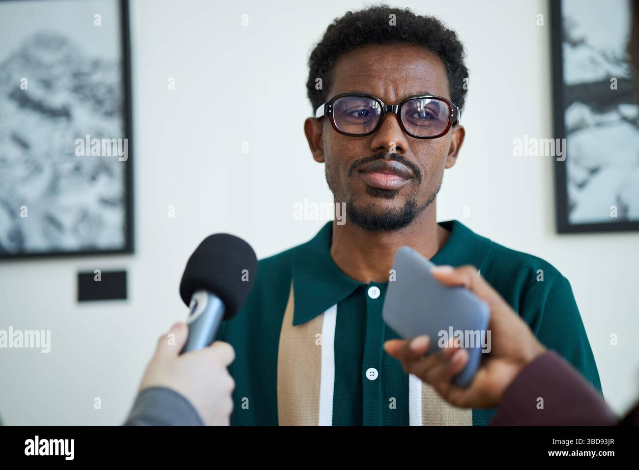 Porträt eines Mannes, der eine Brille trägt, während er von mehreren Reportern befragt wurde, die Mikrofone und Aufnahmegeräte in der Hand halten Stockfoto