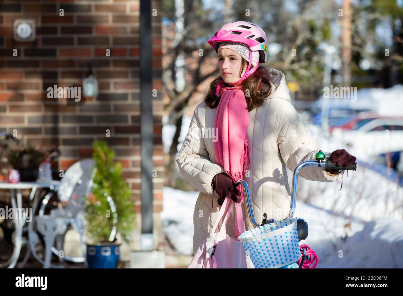 Tween geht mit ihrem Fahrrad nach Hause an einem sonnigen Wintertag in einem finnischen Vorort. Schnee auf dem Boden, ein echter Moment des nordischen Alltags. Stockfoto