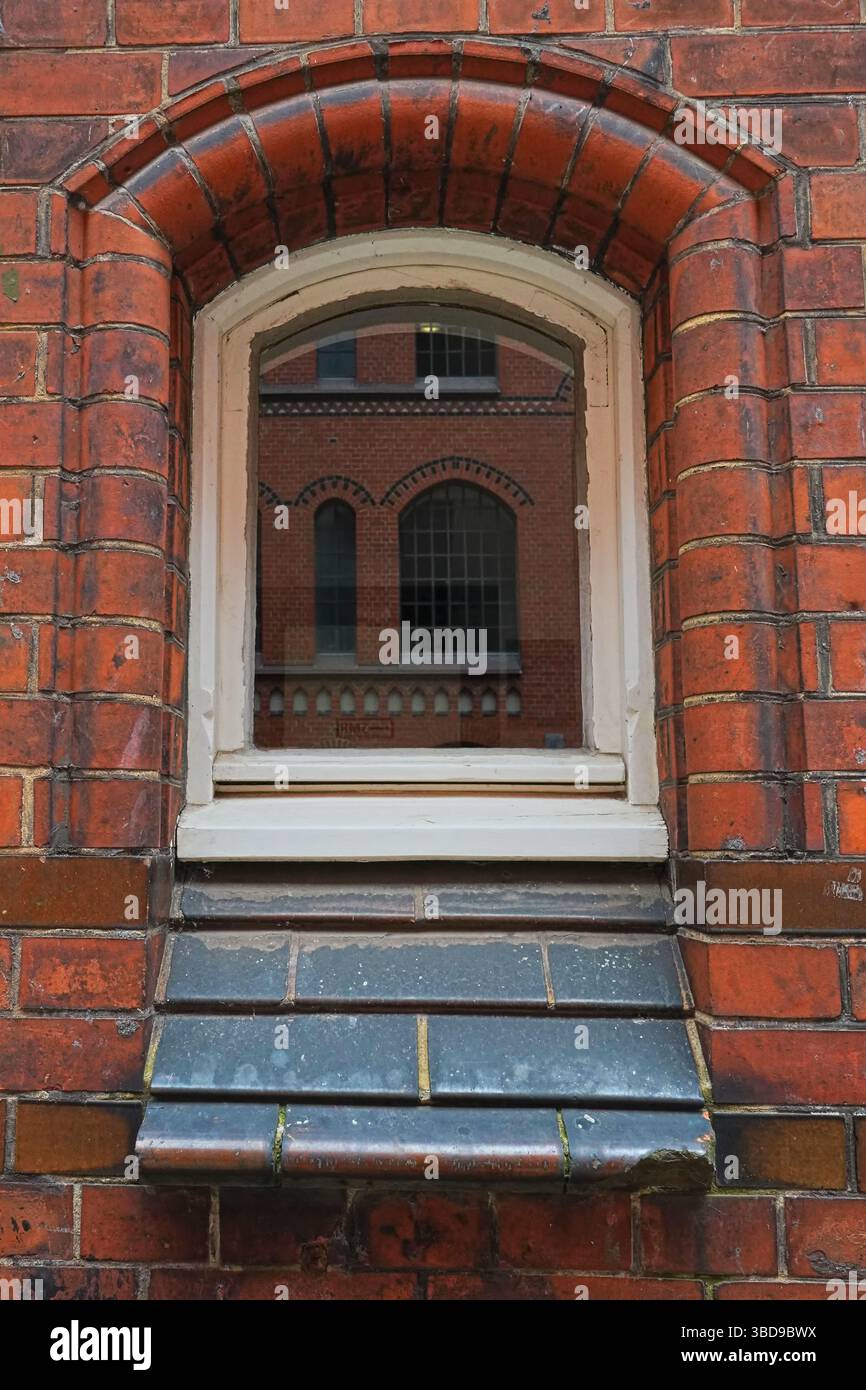 Bogenfenster in roter Backsteinfassade, das das historische Lagerhaus in der Speicherstadt, Hamburg, darstellt, das zum UNESCO-Weltkulturerbe gehört. Stockfoto