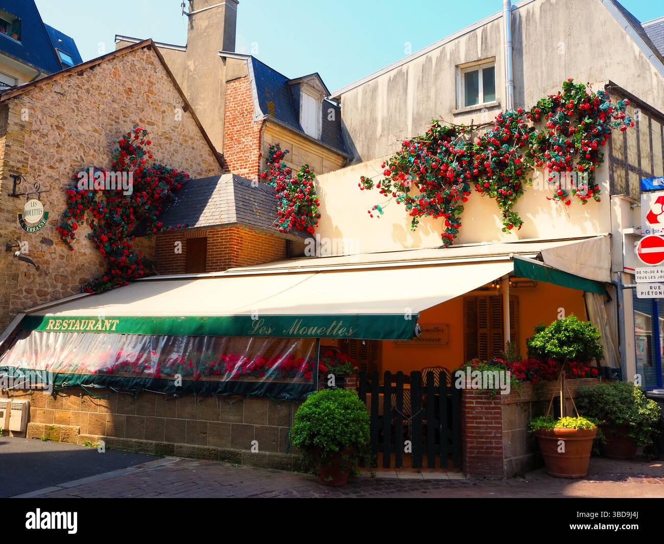 Bezauberndes französisches Restaurant mit roten Blumendekorationen in sanftem Nachmittagslicht Stockfoto