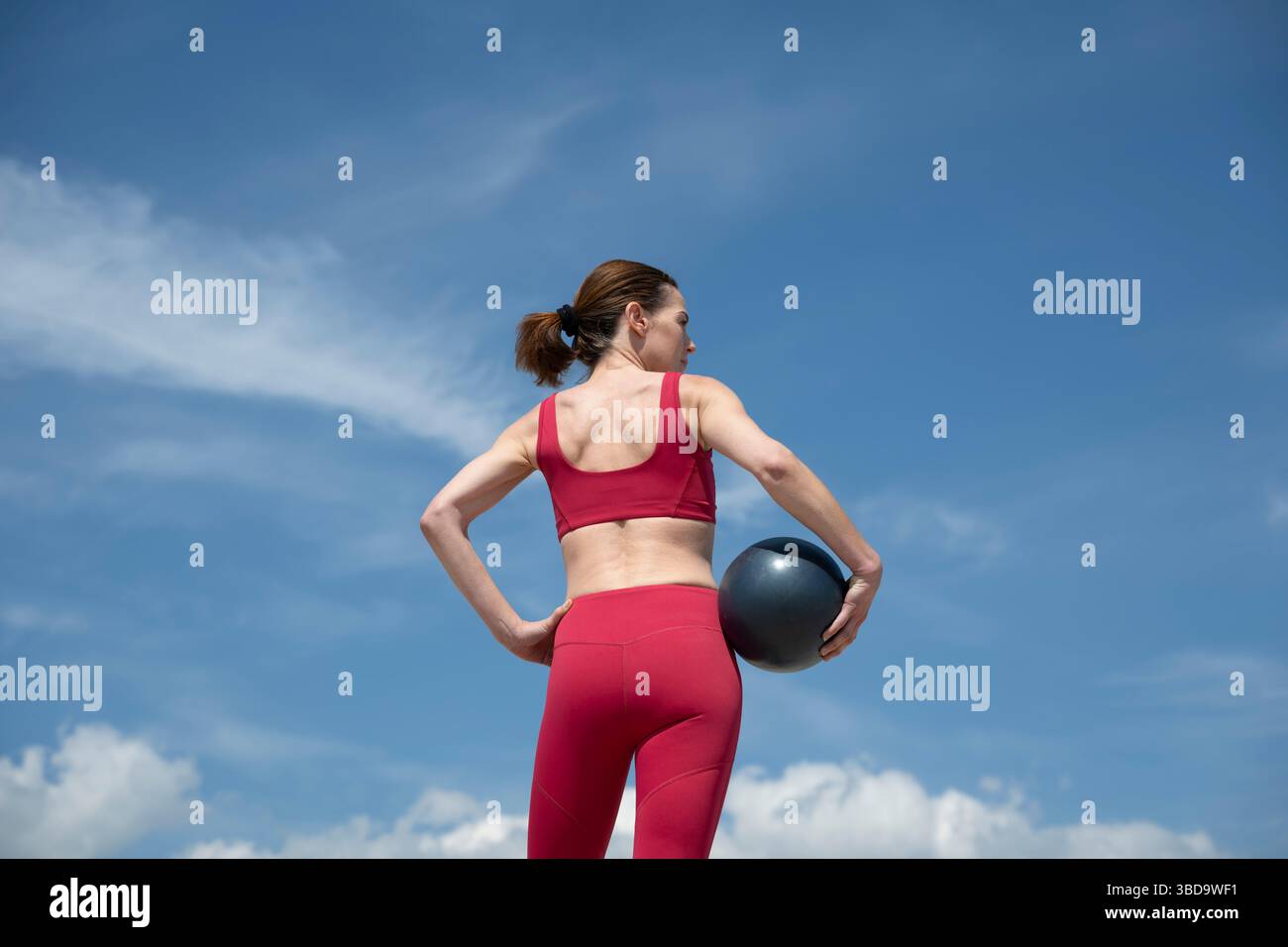 Athletische Frau, die draußen unter dem blauen Himmel Pilates Ball hält Stockfoto