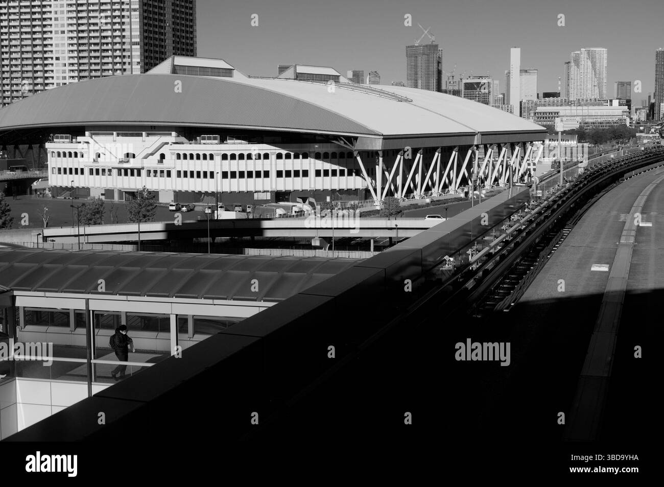 Ein monochromer Blick auf das Ariake Coliseum, eingerahmt von den geschwungenen Spuren der Yurikamome-Linie Stockfoto