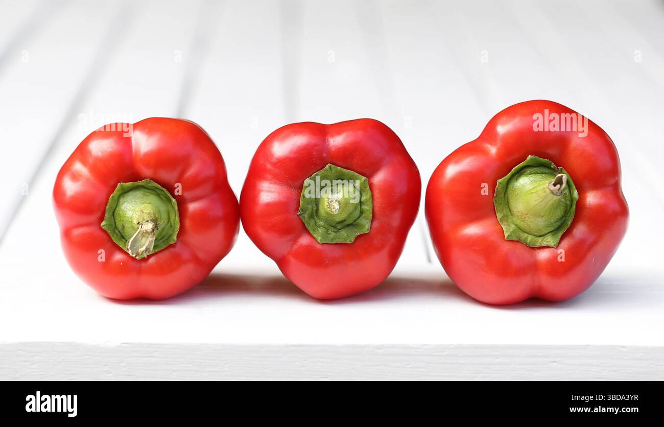 Drei rote Paprika. Frisches Gemüse auf weißem Holz. Gesunde Bio-Lebensmittel Nahaufnahme. Minimale Küchenzusammensetzung. Helle Farbe und Textur. Stockfoto