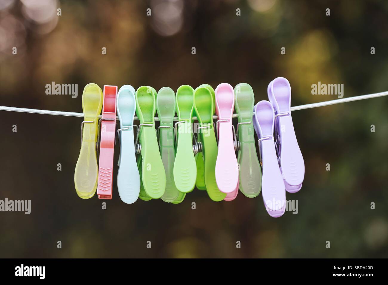 Bunte Plastiklappen am Seil. Hängende Clips im Freien. Wäschekonzept bei Tageslicht. Helle Haushaltsdetails. Mehrfarbige Anordnung der Stifte. Stockfoto