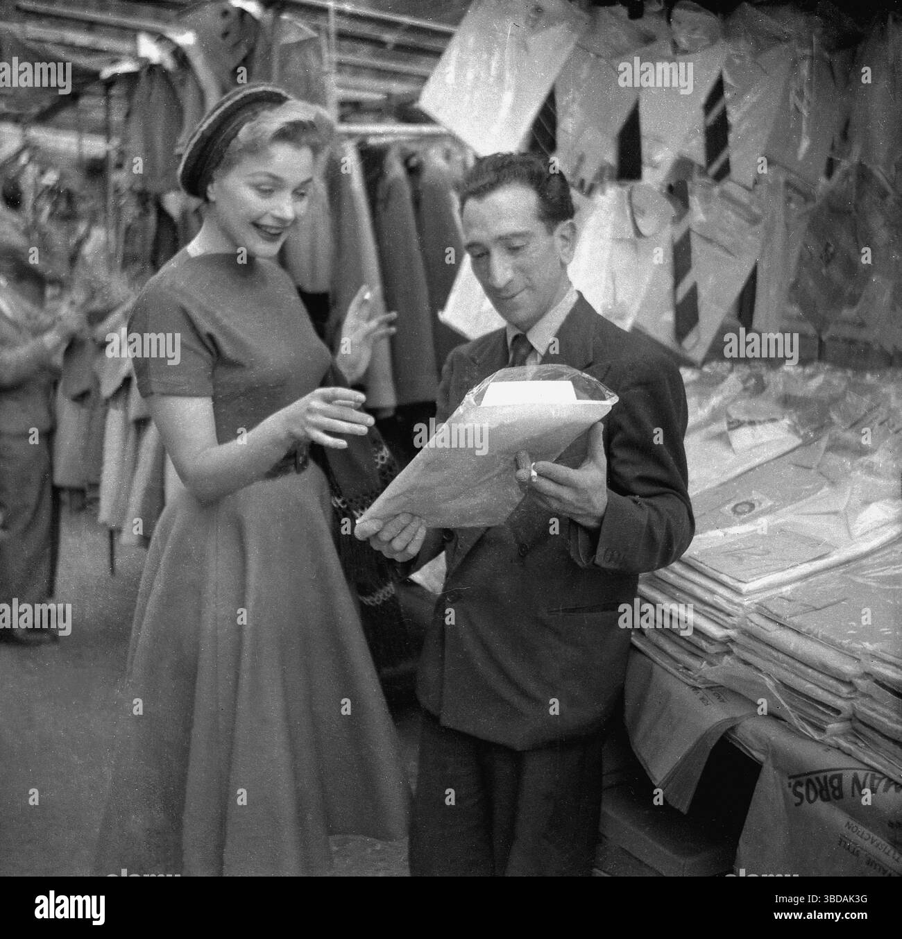 1950er Jahre, historische, elegante junge Dame, Club Row Market, Händler zeigt ihr ein Herrenhemd, East End, London, England, Großbritannien. Stockfoto