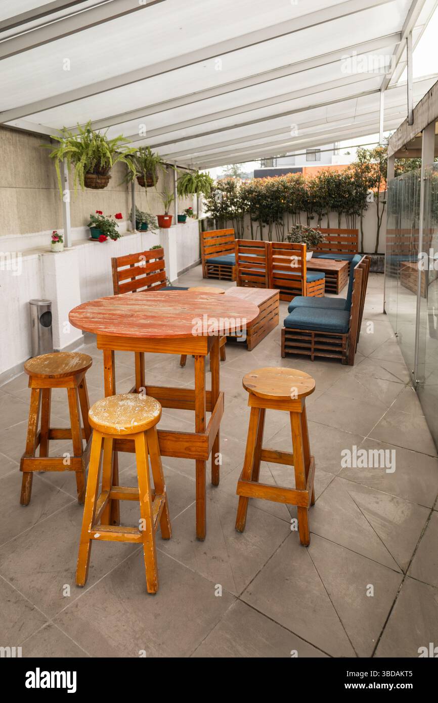 Eine charmante Dachterrasse mit rustikalen Holztischen und -Stühlen, umgeben von Pflanzen und schattigen Baldachin für Komfort und Stil. Stockfoto