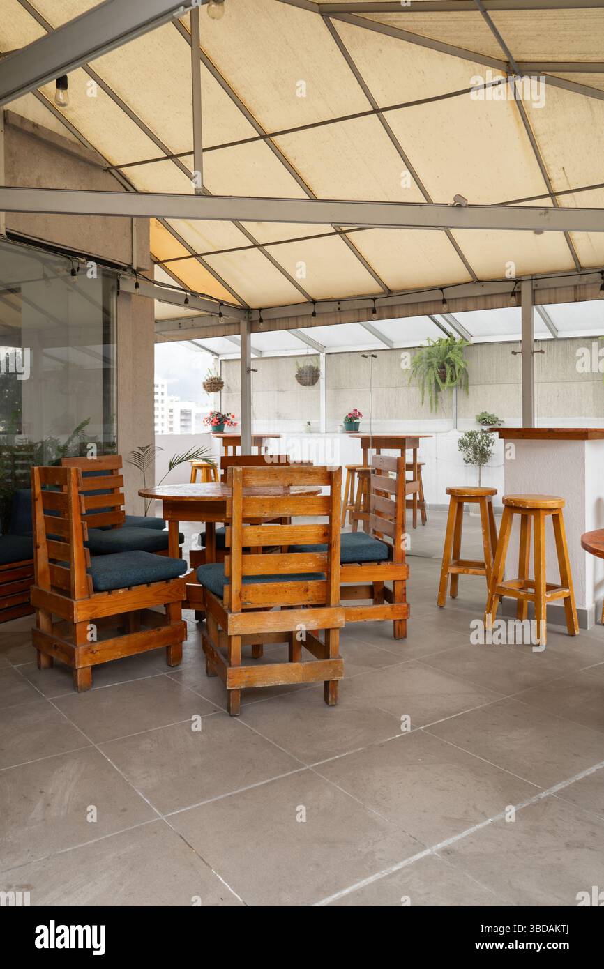 Eine Außenterrasse mit Holztischen und Stühlen mit blauen Kissen unter einem Baldachin schafft eine gemütliche und ungezwungene Atmosphäre für Treffen. Stockfoto