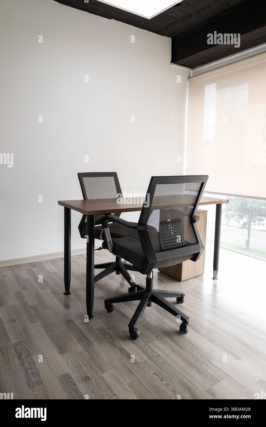 Ein stilvoller, verglaster Tagungsraum mit zwei schwarzen Stühlen und einem kleinen Tisch für professionelle Diskussionen und private Teamarbeit Stockfoto
